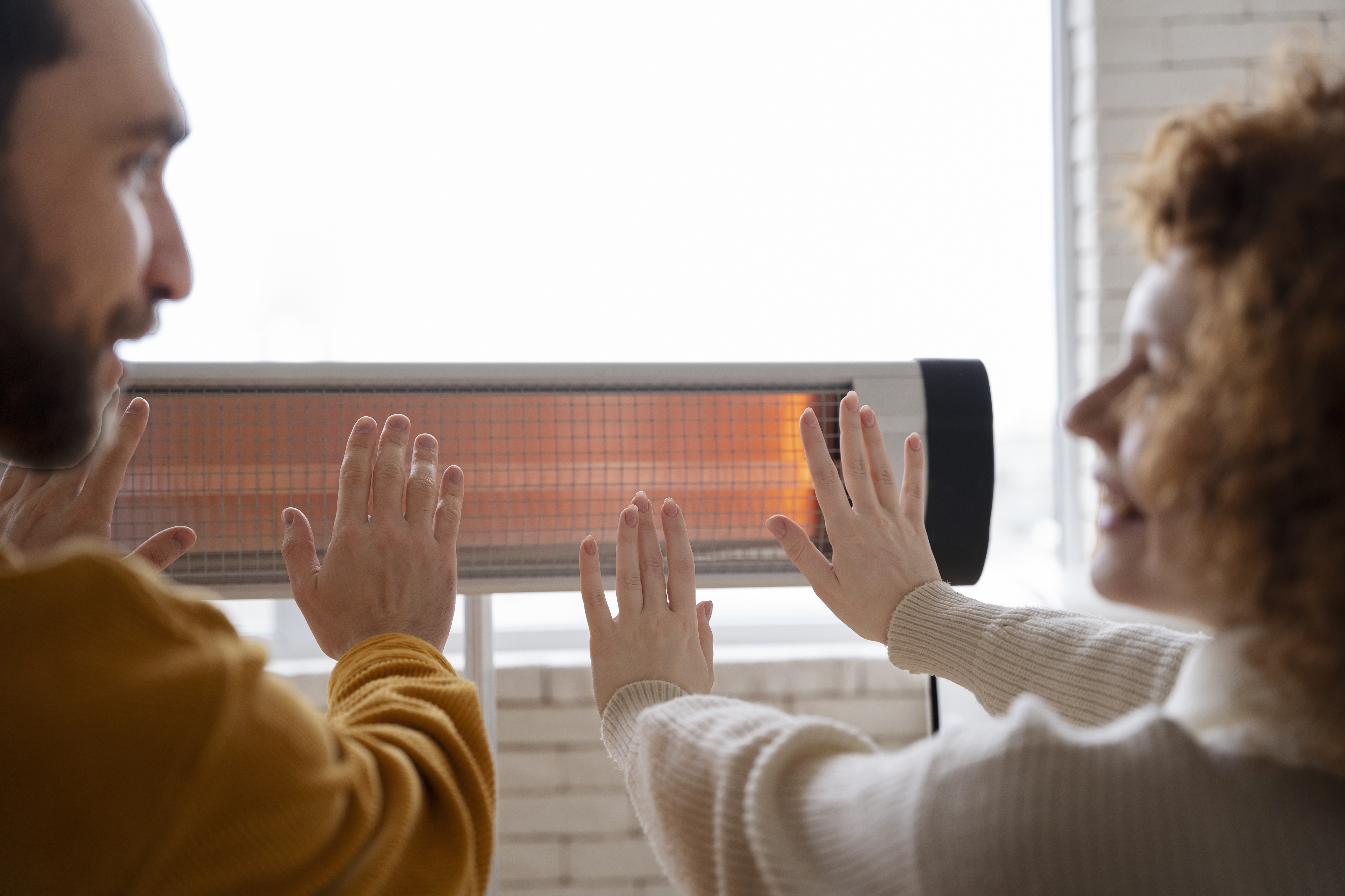 smiley-couple-warming-up-hands-near-heater